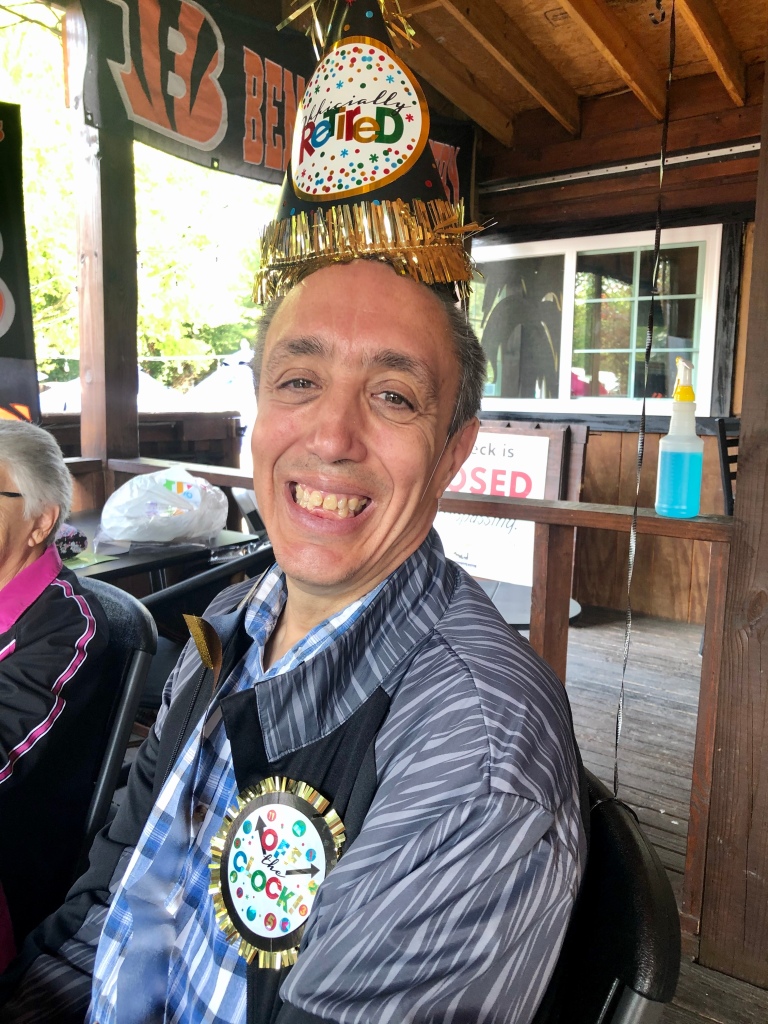 A man has a big smile. He is wearing a party hat that says "officially retired"